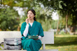 © DragonImages - Pensive medical nurse in scrubs sitting on bench in park and eating lunch