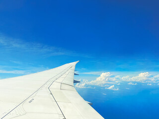 the travel plane flight trip landscape outside airplane window view with fly airplane wing is a white fluffy cloud cloudscape with clear sunny and bright sunlight sky on a blue wide high skyline