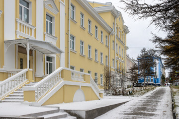 Wall Mural - View of the snow-covered sidewalk and beautiful buildings in the historical center of Magadan. Magadan region, Russia. Cold snowy weather. Autumn in a northern city.