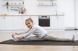 Fitness, little preschool female training yoga in half tortoise pose in kitchen floor at home, copy space. Young slim girl in white sportswear makes stretching training doing splits exercise.