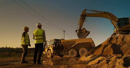 Wall Mural - Caucasian Male Real Estate Investor And Project Manager Talking On Construction Site Of Apartment Block. Colleagues Discussing Building Progress. Excavator Loading Sand In Industrial Truck On Warm Day