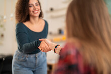 Happy young females in casual clothes smiling and shaking hands while greeting each other during meeting against blurred background