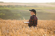 © scharfsinn86 - Woman farmer working with laptop on wheat field. Smart farming and digital agriculture..