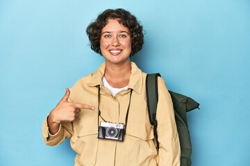 Young traveler woman with vintage camera person pointing by hand to a shirt copy space, proud and confident