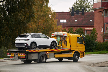 A tow truck carries a car on a flatbed trailer on the highway, providing transport service and assistance after an accident.