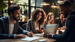 © visoot - Smiling group of diverse business people going over paperwork together and working on a laptop at a table in an office.
