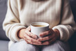 Hands of middle aged caucasian woman is sitting on the sofa with a mug of hot drink