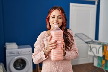 Wall Mural - Young caucasian woman smiling confident smelling detergent bottle at laundry room