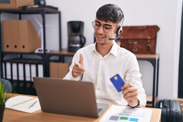 Wall Mural - Young hispanic man working using computer laptop holding credit card pointing fingers to camera with happy and funny face. good energy and vibes.