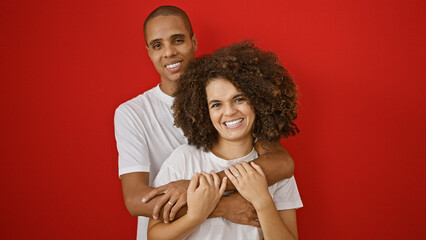 Wall Mural - Beautiful couple expresses love through a confident hug, smiling joyfully over an isolated red background