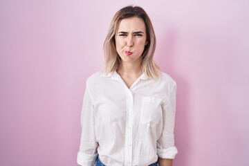 Canvas Print - Young beautiful woman standing over pink background puffing cheeks with funny face. mouth inflated with air, crazy expression.