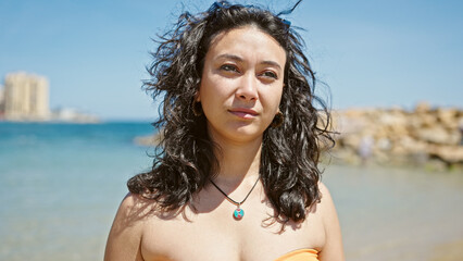 Wall Mural - Young beautiful hispanic woman tourist wearing bikini standing with serious expression at beach