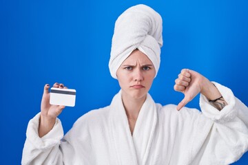 Poster - Blonde caucasian woman wearing bathrobe holding credit card with angry face, negative sign showing dislike with thumbs down, rejection concept