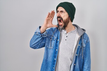 Canvas Print - Young hispanic man with tattoos wearing wool cap shouting and screaming loud to side with hand on mouth. communication concept.