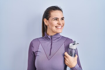 Poster - Beautiful woman wearing sportswear holding water bottle looking away to side with smile on face, natural expression. laughing confident.