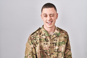 Wall Mural - Young man wearing camouflage army uniform winking looking at the camera with sexy expression, cheerful and happy face.