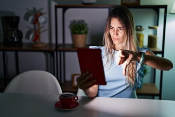 Canvas Print - Young hispanic woman using touchpad sitting on the table at night looking unhappy and angry showing rejection and negative with thumbs down gesture. bad expression.