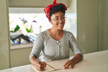 Poster - African american woman writing on notebook sitting on table at home