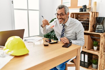 Wall Mural - Middle age grey-haired man architect smiling confident eating sushi at office