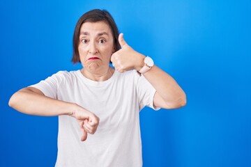 Wall Mural - Middle age hispanic woman standing over blue background doing thumbs up and down, disagreement and agreement expression. crazy conflict