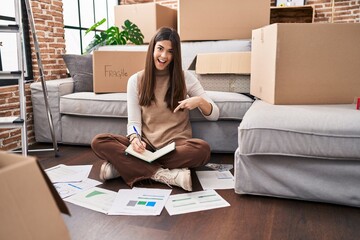 Canvas Print - Young brunette woman moving to a new home doing finances smiling happy pointing with hand and finger