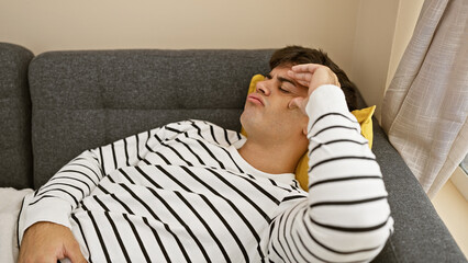 Poster - Stressed young hispanic man alone, grappling with anxiety, lies in despair on his living room sofa at home, a portrait of frustration and sadness