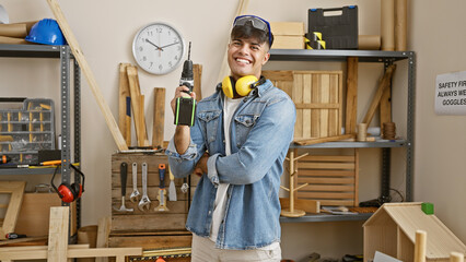 Canvas Print - Young hispanic man carpenter wearing glasses and headphones holding drill at carpentry