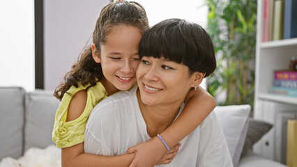 Wall Mural - Confident mother and daughter sharing a joyful hug, smiling heartily while sitting on the living room sofa at home â€“ a beautiful expression of family love and happiness