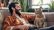 © IndigoElf - Young man in modern clothes sit on a living room couch with his domestic cat. Cozy room interior design. Smiling cheerful man love his cat.