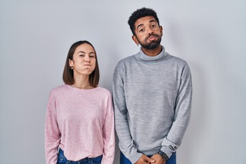 Canvas Print - Young hispanic couple standing together puffing cheeks with funny face. mouth inflated with air, crazy expression.