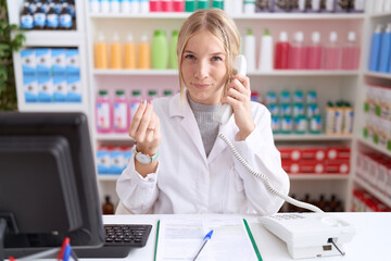 Poster - Young caucasian woman working at pharmacy drugstore speaking on the telephone doing money gesture with hands, asking for salary payment, millionaire business