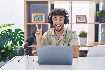 Canvas Print - Arab man with beard working at the radio smiling with happy face winking at the camera doing victory sign. number two.