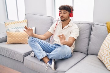 Poster - Young arab man doing yoga exercise sitting on sofa at home