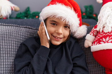 Canvas Print - Adorable hispanic boy talking on smartphone sitting on sofa by christmas decoration at home