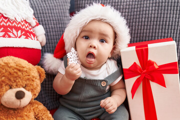 Sticker - Adorable hispanic toddler sitting on sofa wearing christmas hat at home