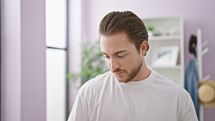 Wall Mural - Young hispanic man looking down with serious expression at home