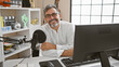 © Krakenimages.com - Young, attractive, grey-haired hispanic man smiling and masterfully presenting news on a live radio show inside a professional radio studio