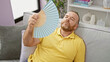 © Krakenimages.com - Middle-aged caucasian man suffering in hot weather, fanning himself with handfan while sitting on sofa at home