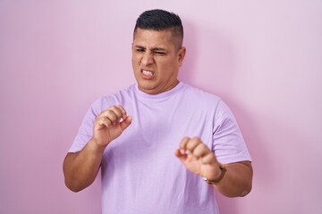 Wall Mural - Young hispanic man standing over pink background disgusted expression, displeased and fearful doing disgust face because aversion reaction.