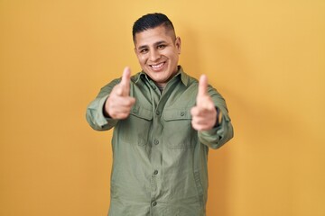 Sticker - Hispanic young man standing over yellow background pointing fingers to camera with happy and funny face. good energy and vibes.