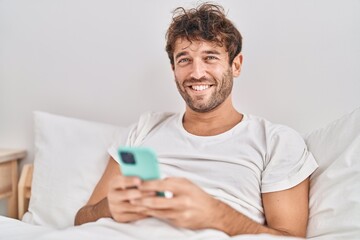 Poster - Young man using smartphone sitting on bed at bedroom