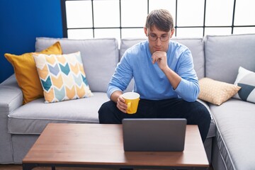 Wall Mural - Young caucasian man using laptop drinking coffee at home