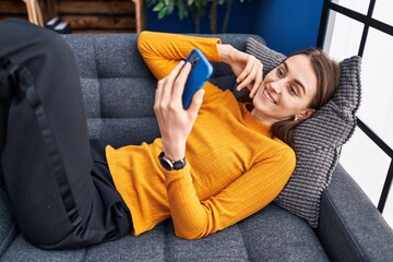 Wall Mural - Young caucasian woman using smartphone lying on sofa at home