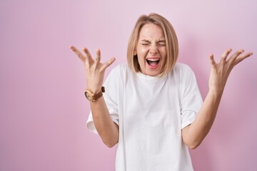 Poster - Young caucasian woman standing over pink background celebrating mad and crazy for success with arms raised and closed eyes screaming excited. winner concept