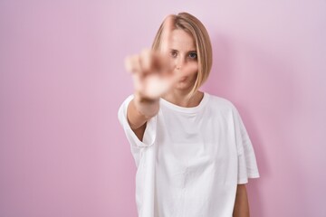 Sticker - Young caucasian woman standing over pink background pointing with finger up and angry expression, showing no gesture