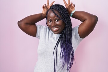 Wall Mural - Young african woman standing over pink background posing funny and crazy with fingers on head as bunny ears, smiling cheerful