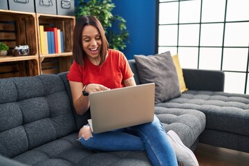 Sticker - Young hispanic woman using laptop at home smiling happy pointing with hand and finger