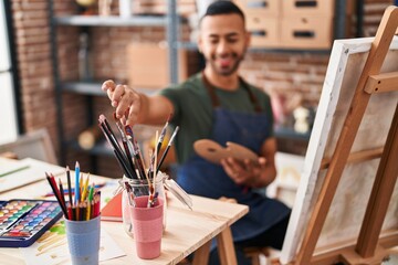 African american man artist smiling confident holding paintbrush at art studio