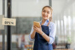 © David - Happy SME business barista cafe owner Asian woman waitress apron and staning at the door with a sign Open waiting for customers , cafes and restaurants entrepreneur Small business concept.