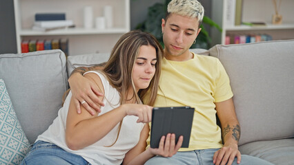 Wall Mural - Beautiful couple using touchpad sitting on sofa at home